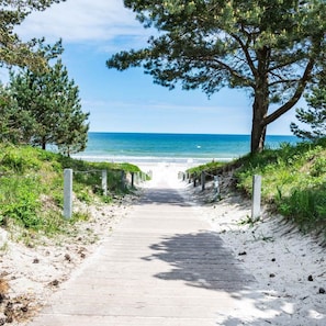 Ein hölzerner Weg führt zu einem Strand mit freiem Blick auf das Meer.