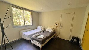A small, single-room hotel room with a bed, a window, a radiator, and a door. - Grand French Family Holiday Home (Saint-Germain-sur-Bresle)