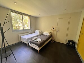 Ein kleines Hotelzimmer für eine Person, mit Bett, Fenster, Heizkörper und Tür.