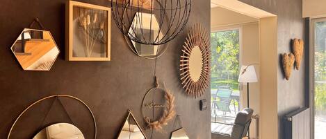 A modern interior with a variety of wall-mounted mirrors and decorative items, a seating area with a chair, and a view of an outdoor patio.