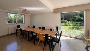 A spacious dining area with a long wooden table and modern chairs, large windows, and a view of a garden. - Grand French Family Holiday Home (Saint-Germain-sur-Bresle)