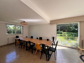 Ein geräumiger Essbereich mit einem langen Holztisch, modernen Stühlen, großen Fenstern und Blick auf einen Garten.