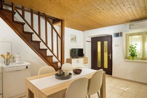 A dining area with a wooden table, chairs, a staircase, a television, and a kitchen area with a dishwasher. - Eco friendly holiday home with pool (Pula)