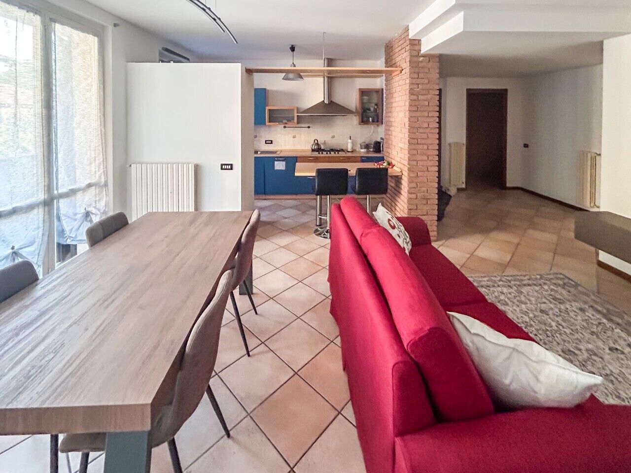 A modern living space with a dining area, a red sofa, and a kitchen in the background.