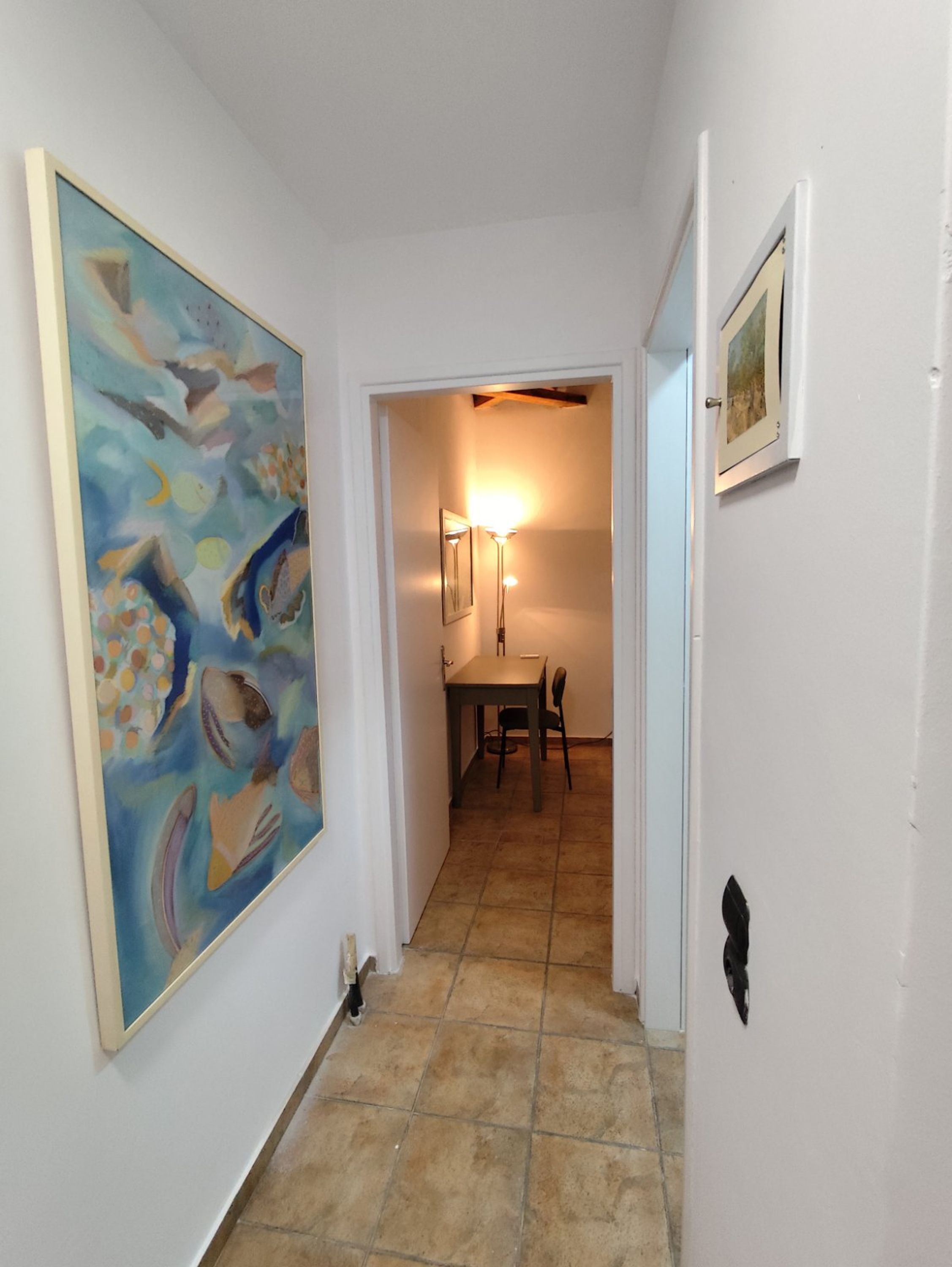 Un corridoio con pavimento piastrellato, una zona pranzo con tavolo e sedie e un quadro appeso al muro.