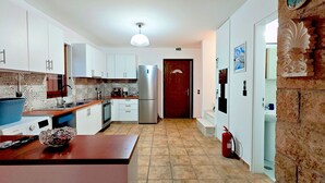 A kitchen with white cabinets, a stainless steel refrigerator, and a tiled floor. - Emmelia Stone Maisonette: Panoramic Sea View (Kalamata)