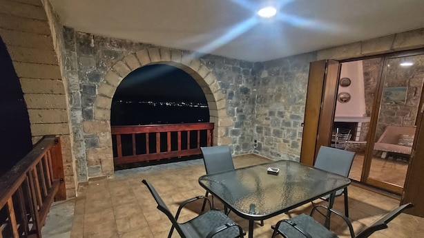 An outdoor patio with a stone wall, a glass table, and metal chairs. - Emmelia Stone Maisonette: Panoramic Sea View (Kalamata)