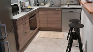 Una cocina moderna con armarios de madera, una campana extractora de acero inoxidable, lavavajillas, microondas y cafetera.