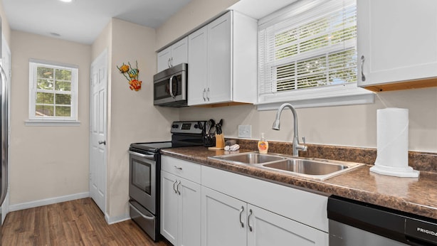 A kitchen with white cabinets, a stainless steel sink, a microwave, and a dishwasher. - Pond View Escape - Resort Access (Branson)