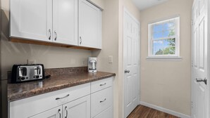 A kitchen with white cabinets, a toaster, a coffee maker, and a window with blinds. - Pond View Escape - Resort Access (Branson)
