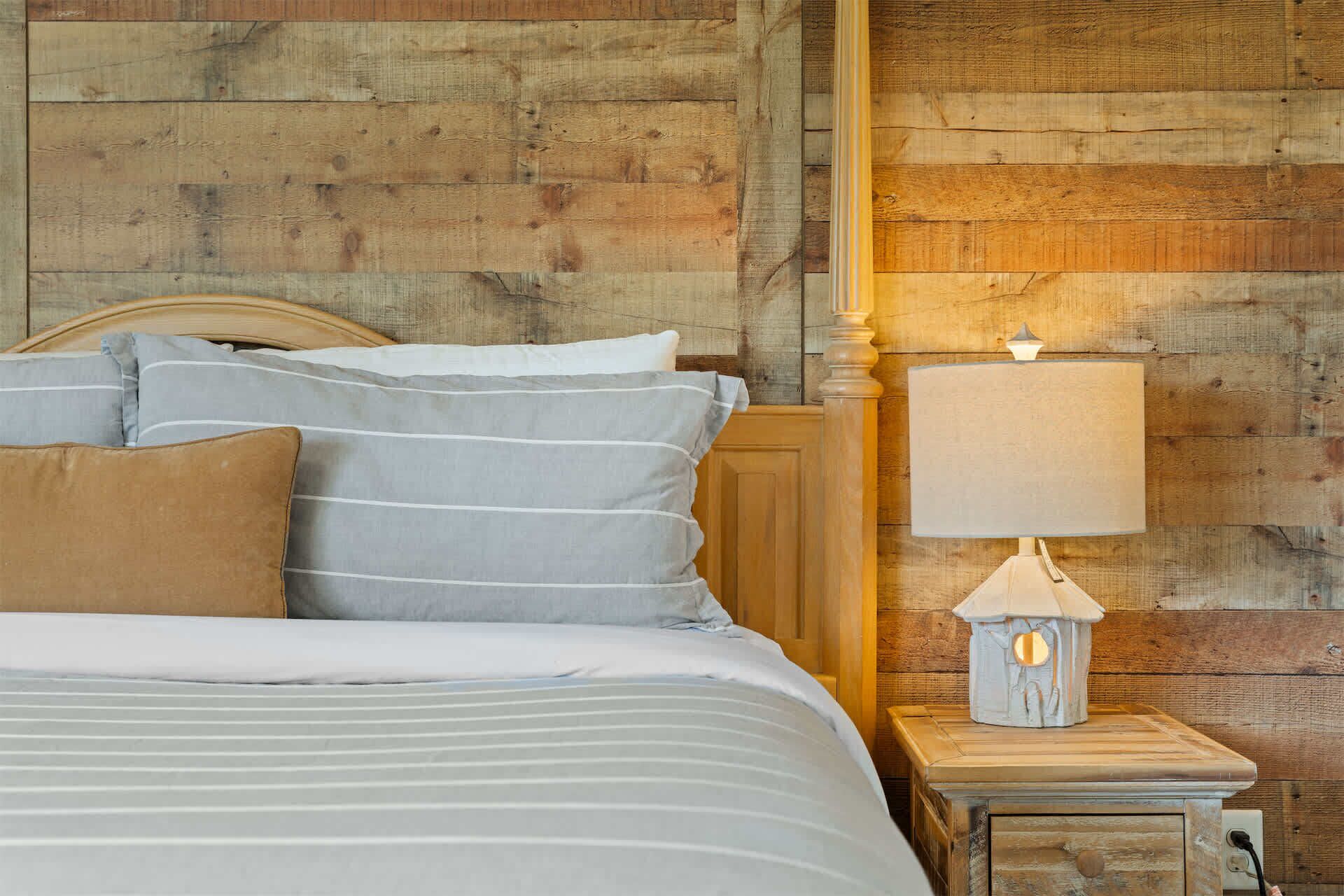 A bed with striped bedding, a wooden headboard, and a nightstand with a lamp.