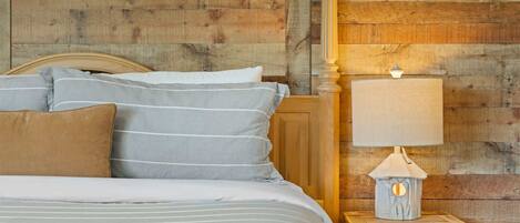 Una cama con ropa de cama a rayas, un cabecero de madera y una mesita de noche con una lámpara.