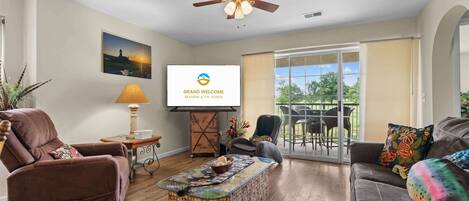 Un salon spacieux doté d’un ventilateur de plafond, d’un téléviseur diffusant l’émission « GRAND WELCOME BRANSON & THE OZARKS », d’un canapé confortable, d’une table basse et d’un balcon aménagé avec du mobilier d’extérieur.