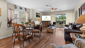 A spacious living room with a dining area, a ceiling fan, and a large screen displaying 'GRAND WELCOME.' - Pond View Escape - Resort Access (Branson)