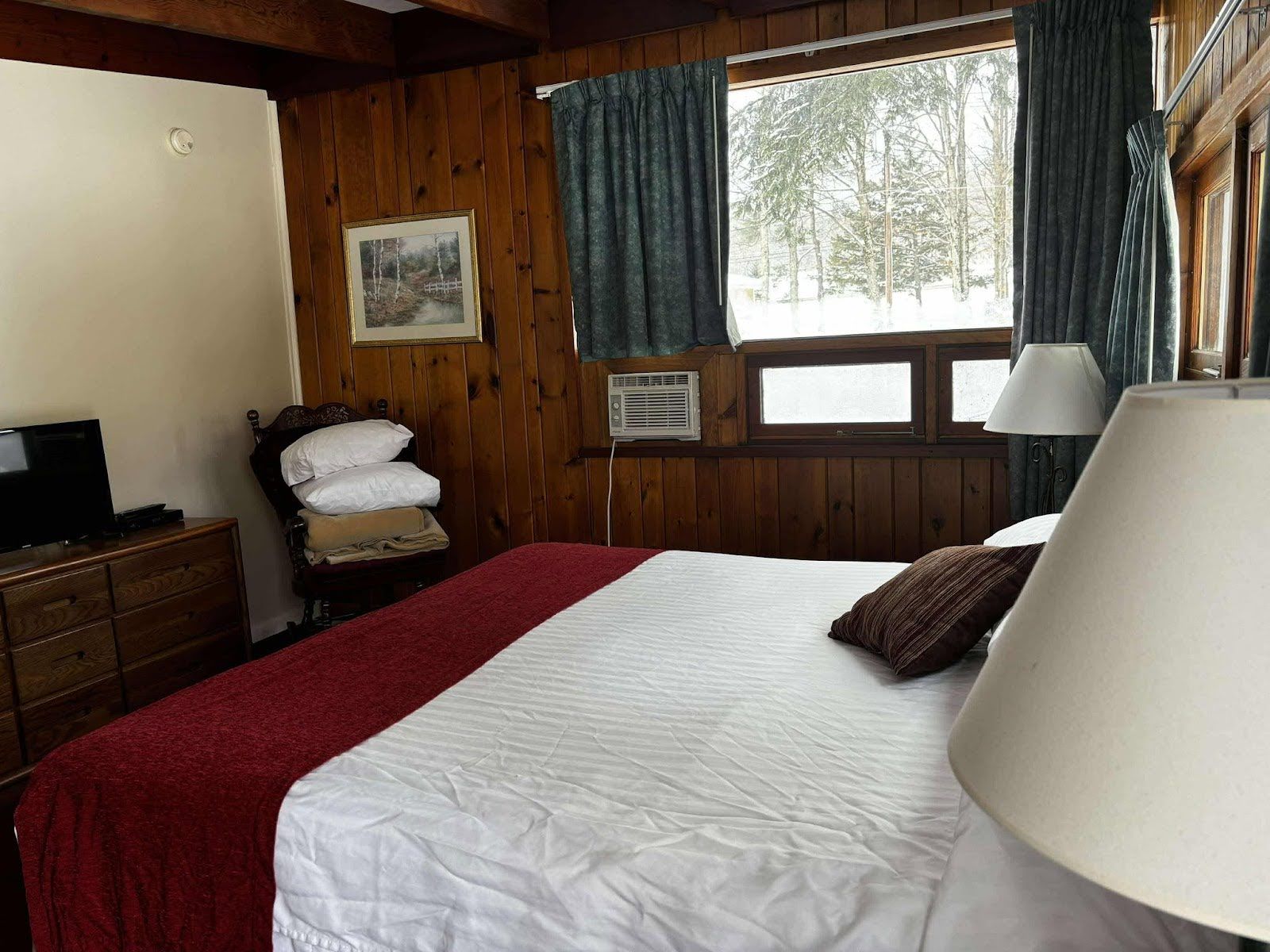 Ein Zimmer mit einem Bett, einem Schminktisch, einem Fenster mit Vorhängen, einem Bild an der Wand und einer Lampe.