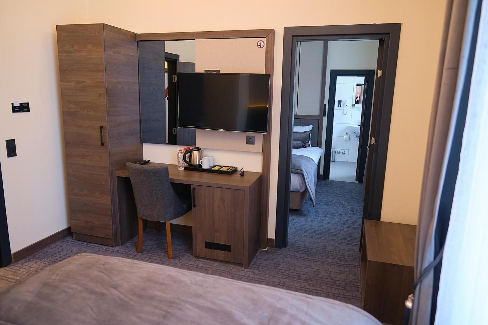 A hotel room with a bed, a desk, a chair, a television, and a bathroom visible through an open door.