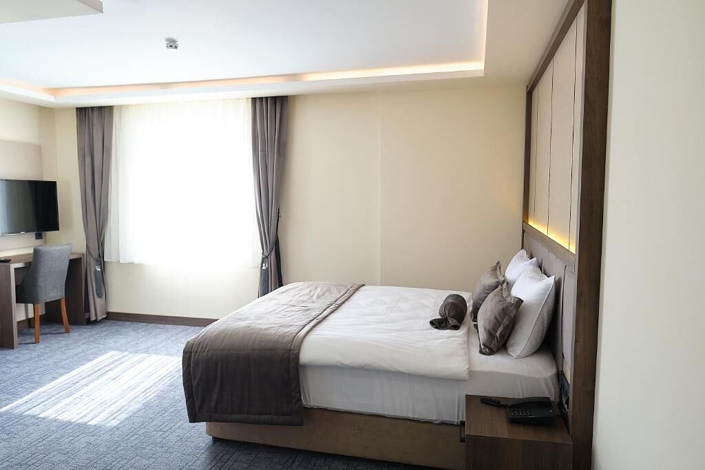 Une chambre d’hôtel avec un lit, un bureau, une chaise, une télévision et une fenêtre avec des rideaux.