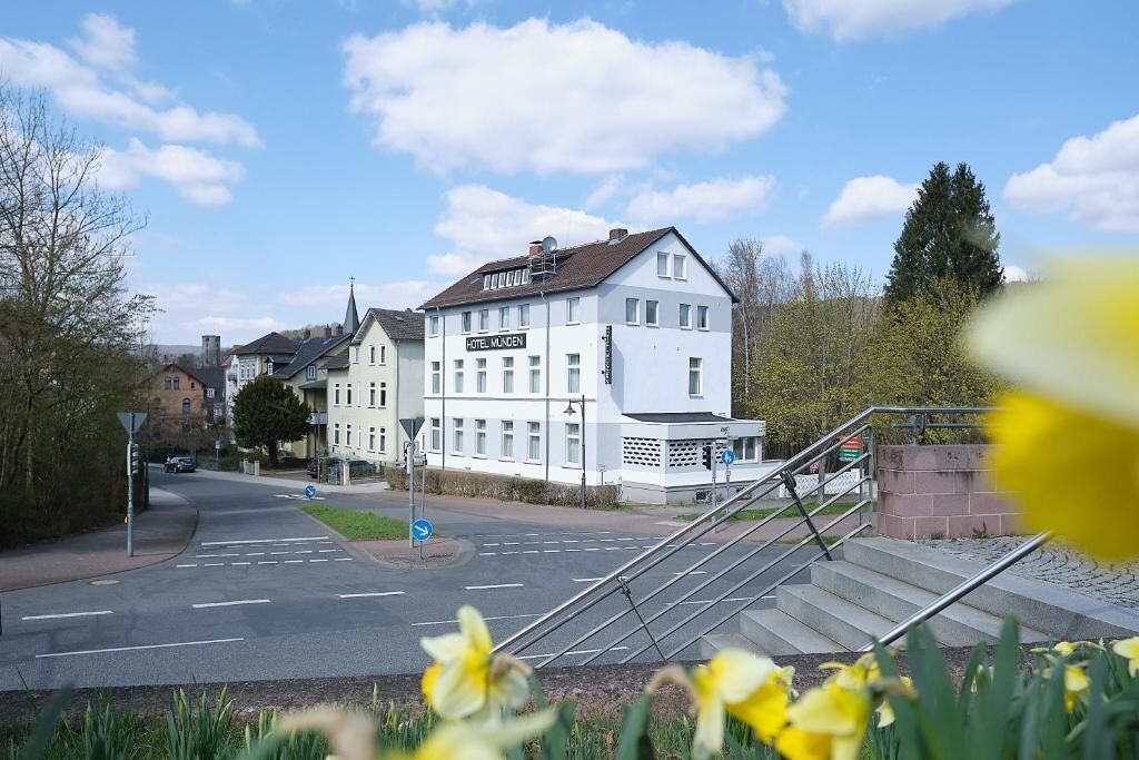 A hotel with a sign 'HOTEL MÜNEN' on a white building with a modern design, located at a street intersection with a pedestrian staircase.