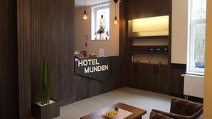 Zona de recepción de un hotel con un mostrador de madera, un cartel que dice 'HOTEL MUNDEN' y una ventana con vistas.