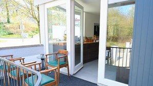 Un balcón con sillas y una mesa, una puerta corrediza de vidrio que da a una cocina y vistas al exterior.