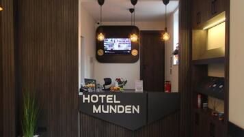 Ein Hotelrezeptionstresen mit einem digitalen Bildschirm, zwei Pendelleuchten und einem Schild mit der Aufschrift 'HOTEL MUNDEN'.