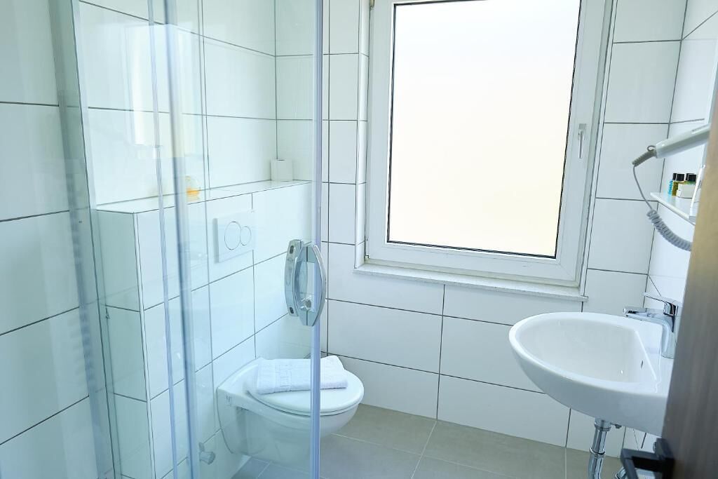 Un bany amb una cabina de dutxa de vidre, un vàter blanc i un lavabo amb una finestra a sobre.