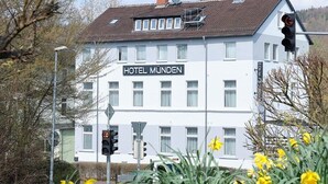 Un edificio blanco con el letrero 'HOTEL MÜNDEN', varias ventanas y un semáforo al frente.