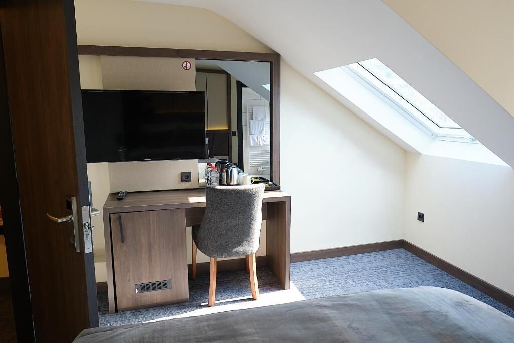 Een slaapkamer met dakraam, een bed, een bureau met stoel en een televisie.