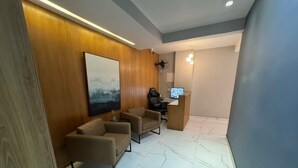 Ein modernes Zimmer mit einer Holzwand, einem großen abstrakten Gemälde, zwei Ledersofas, einem Schreibtisch mit einem Computer und einem Marmorboden.