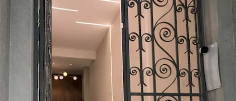 Un pasillo con una reja metálica decorativa, una escalera y un área de recepción al fondo.