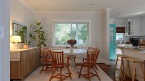 A dining area with a round table, wooden chairs, a potted plant, and a window with blinds. - Beautiful Avondale Bungalow, Downtown BHAM a 5 min drive, UAB & Airport 10 mins. (Birmingham)