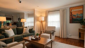 A modern living room with a sofa, armchair, coffee table, and a painting of Birmingham. - Beautiful Avondale Bungalow, Downtown BHAM a 5 min drive, UAB & Airport 10 mins. (Birmingham)