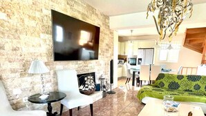 Ein Wohnzimmer mit Flachbildfernseher, einem gemusterten Sofa, einem Couchtisch und einer Deckenleuchte.