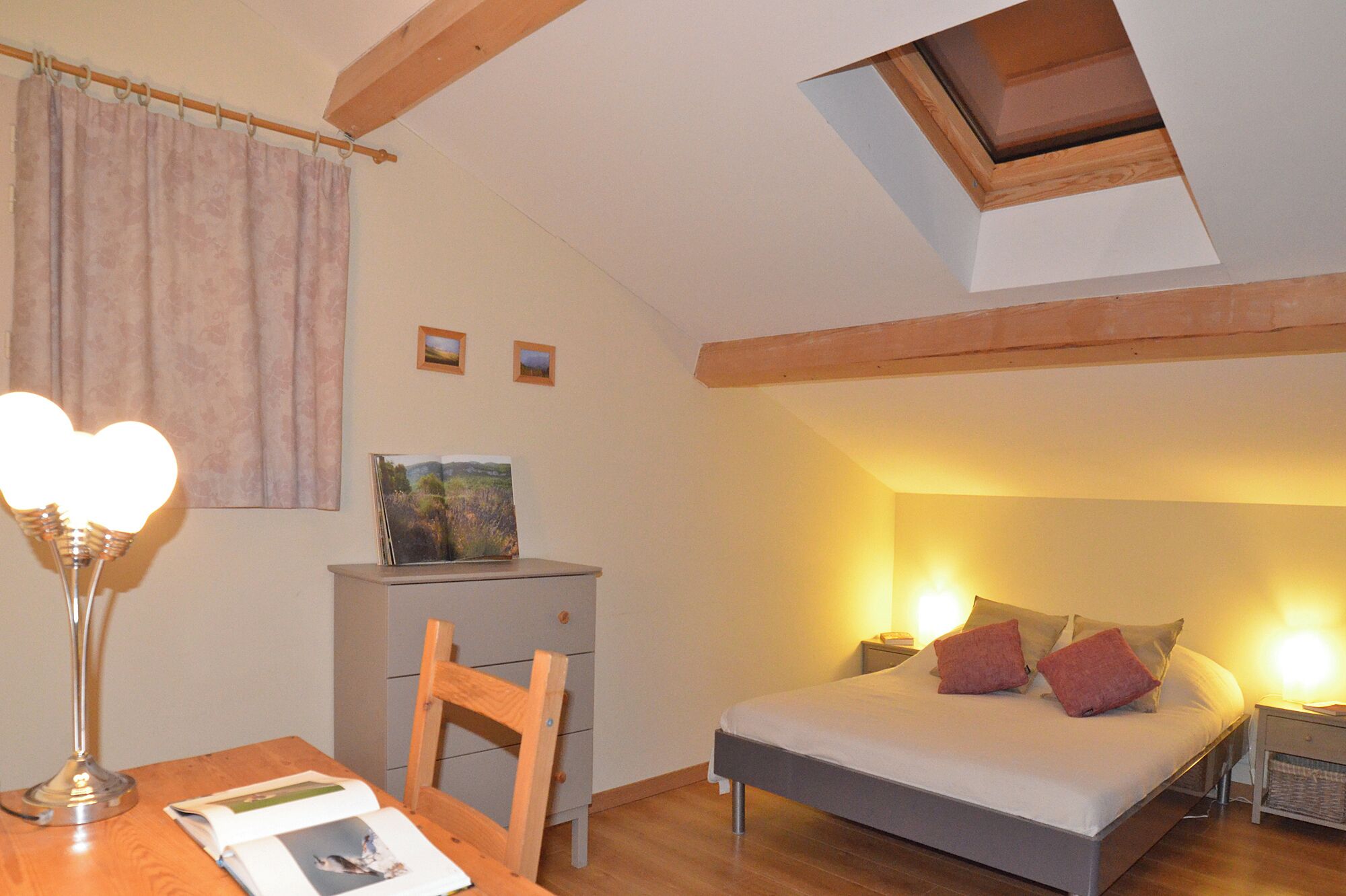 Quarto com cama, mesas de cabeceira, escrivaninha, cadeira, abajur, janela e claraboia.