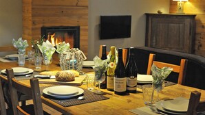 Une table à manger dressée avec des assiettes, des couverts, des bouteilles de vin et des verres, avec une cheminée en arrière-plan.
