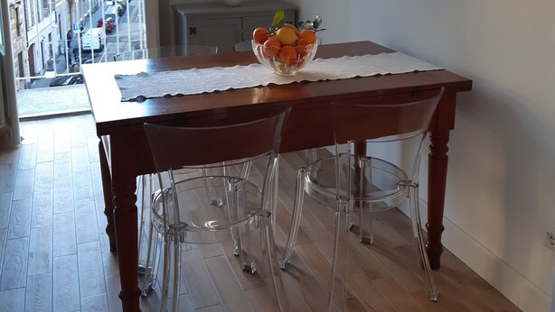 A dining area with a wooden table, clear chairs, a fruit bowl, and wall art. - Vacation in Turin, just a few minutes from downtown in a lively, multicultural neighborhood (Torino)