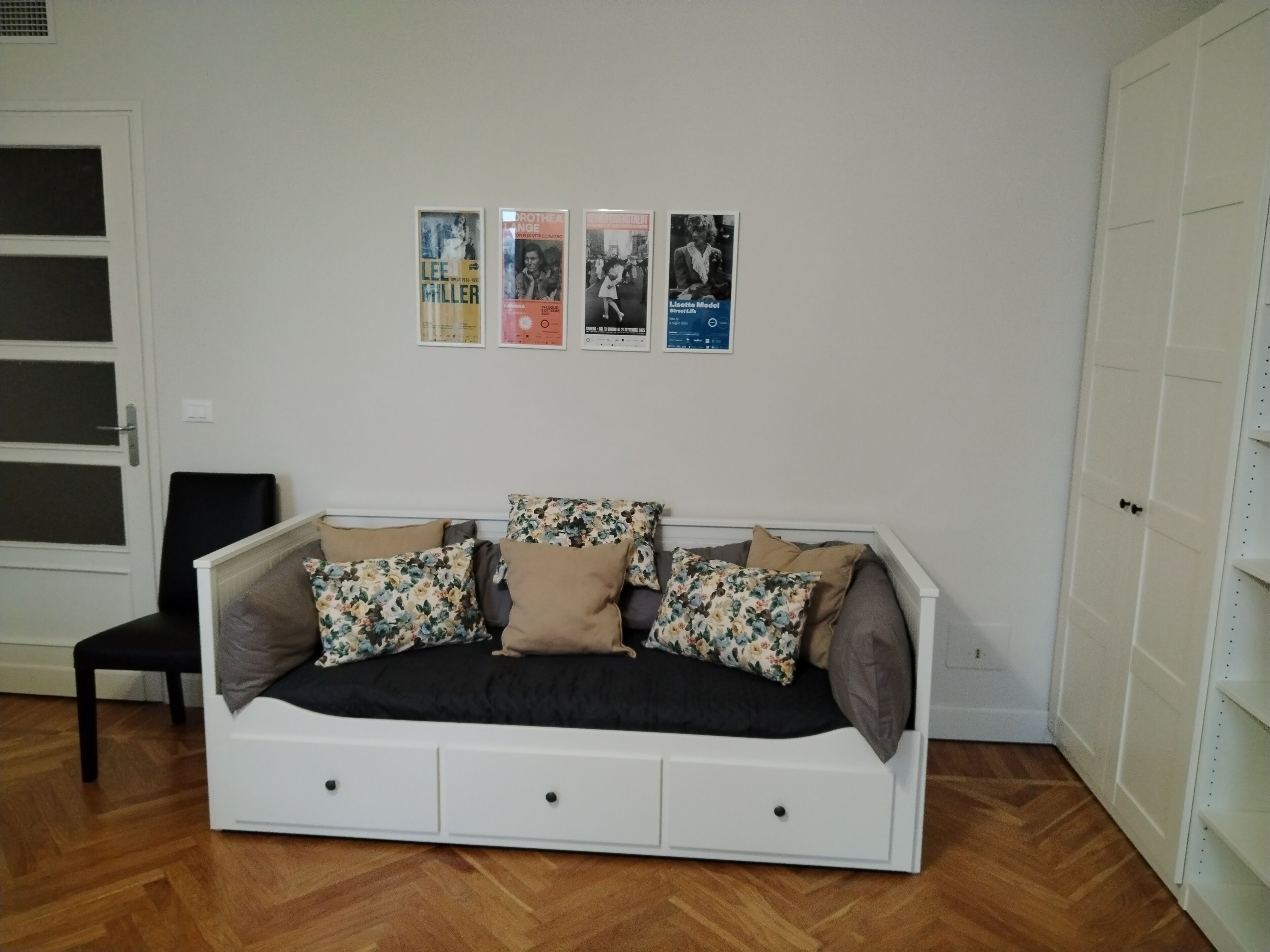 A bedroom with a bed, a chair, and three posters on the wall.