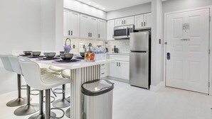 A modern kitchen with white cabinets, stainless steel appliances, and a bar area with stools. - Disney Area Suite w/ Pool & Full Kitchen (Orlando)