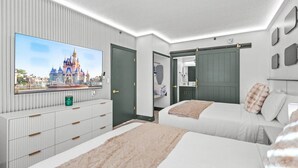 A hotel room with a large TV, two beds, a wardrobe, and a bathroom with a mirror. - Staysky Suite Near Universal & Disney Parks (Orlando)