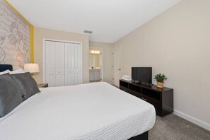 A hotel room with a bed, a TV, a dresser, a mirror, and a bathroom visible in the background. - 6BR Championsgate Home · Pool · Near Disney (Davenport)