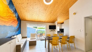 Un interior moderno con techo de madera, una zona de comedor con sillas amarillas, un sofá y un televisor montado en la pared.