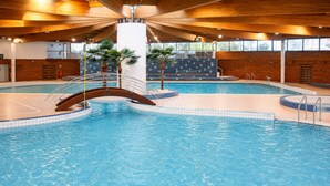 Una piscina interior con un puente de madera, palmeras y suelo de baldosas.