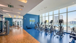 Ein Fitnessstudio mit Cardiogeräten, einer blauen Wand mit motivierenden Texten und großen Fenstern mit Blick auf die Stadt.