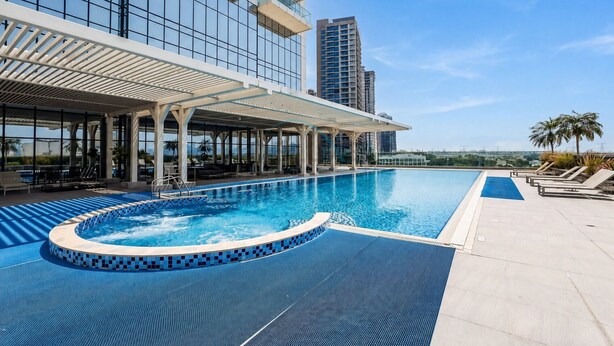 Una piscina con un jacuzzi integrado, sillas de descanso y una zona de estar cubierta con vistas al horizonte de la ciudad.
