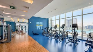 Un gimnasio con equipamiento de cardio, una pared azul con texto motivacional y amplios ventanales con vista a la ciudad.