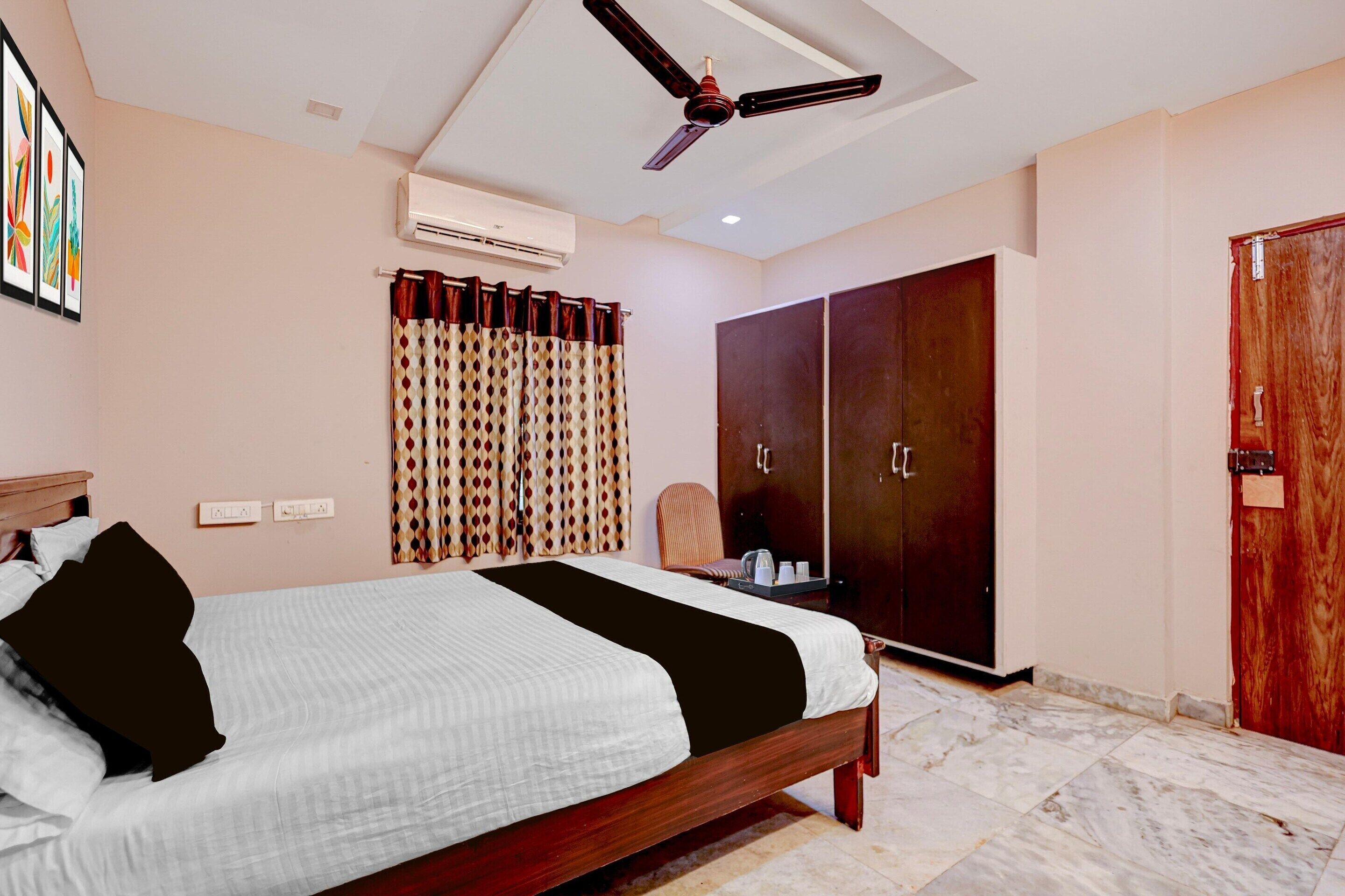 Een hotelkamer met een bed, een kledingkast, een plafondventilator, een airconditioning en een raam met gordijnen.