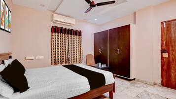 Een hotelkamer met een bed, een kledingkast, een plafondventilator, een airconditioning en een raam met gordijnen.