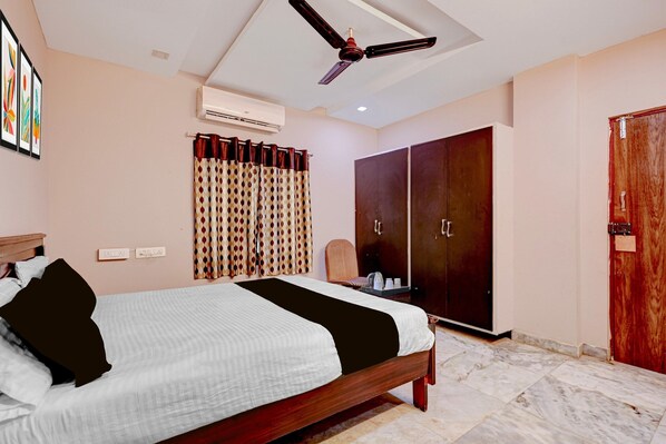 A hotel room with a bed, a wardrobe, a ceiling fan, an air conditioning unit, and a window with curtains.