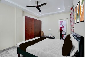Ein Hotelzimmer mit Bett, Sessel, Schreibtisch mit Wasserkocher, Kleiderschrank und Deckenventilator.
