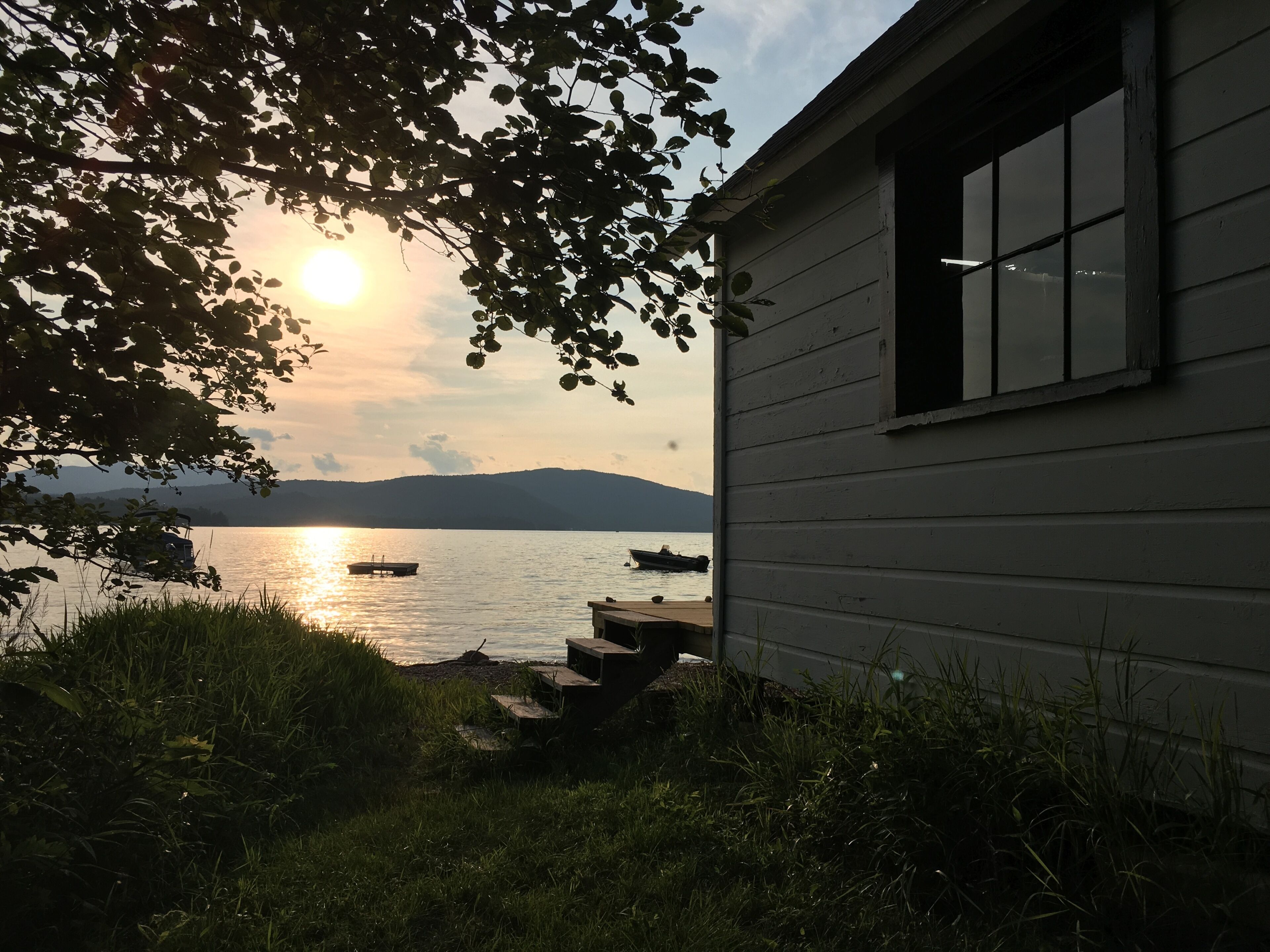 A cabin with a view of a lake and boats, surrounded by grass and trees.